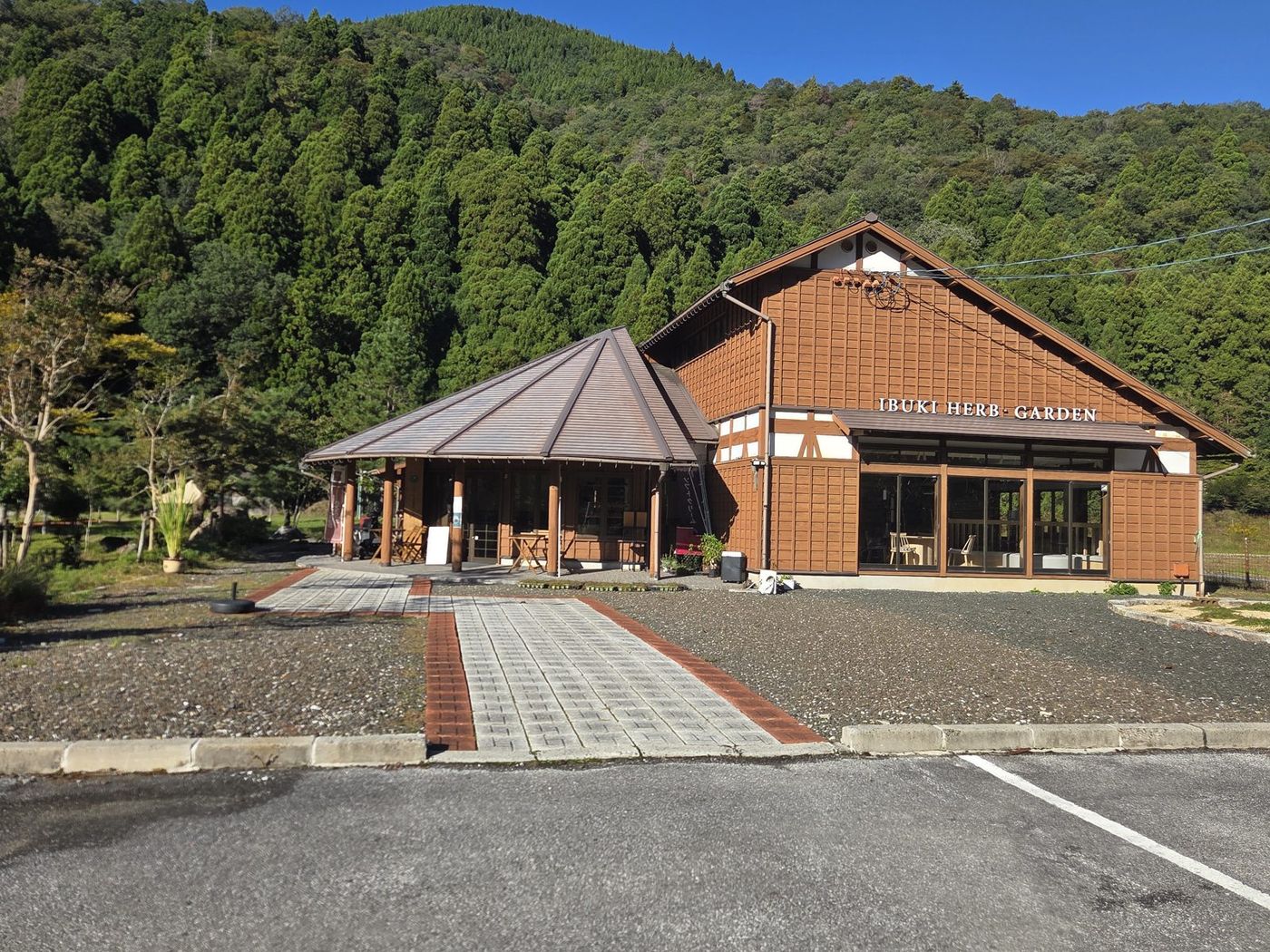 石畳の道の先、屋根のある入口と木造の建物。壁に「IBUKI HERB GARDEN」の文字